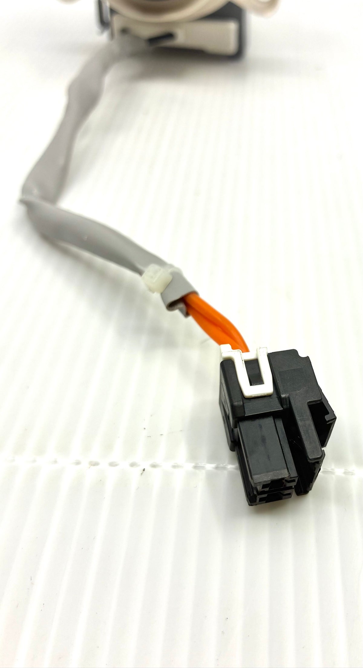 Close-up of drain pump 2-pin locking connector with orange wires and grey sheathed harness lead