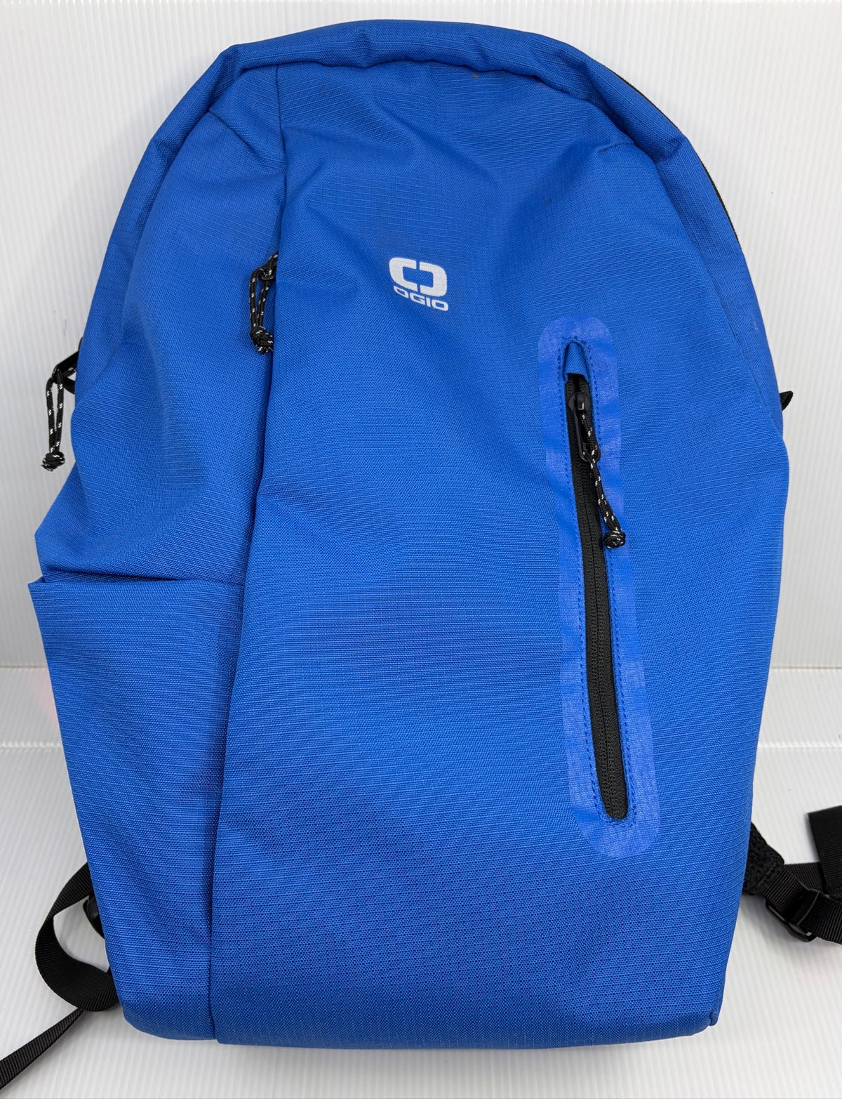 OGIO Shadow backpack in blue, front view showing white OGIO logo, vertical fleece-lined zip pocket and side slip pocket