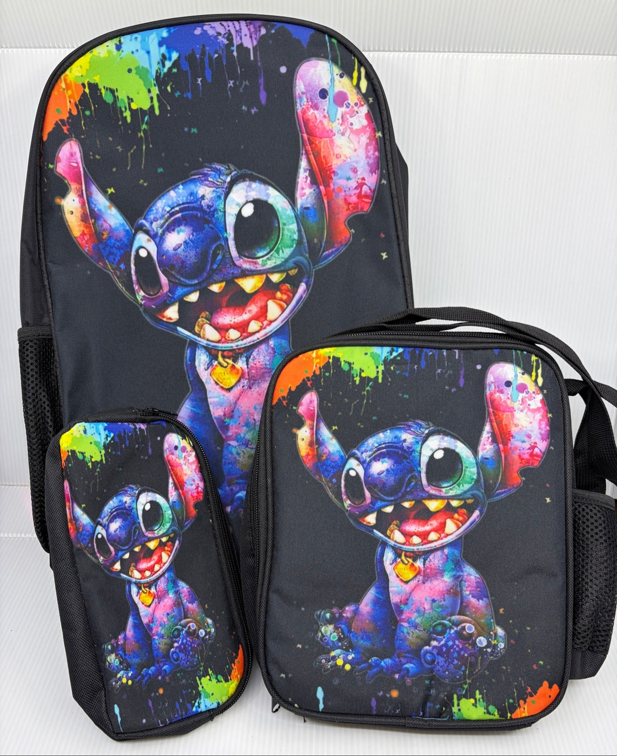 Stitch paint splatter 3-piece backpack set grouped together - backpack, lunch bag and pencil case in rainbow watercolor on black