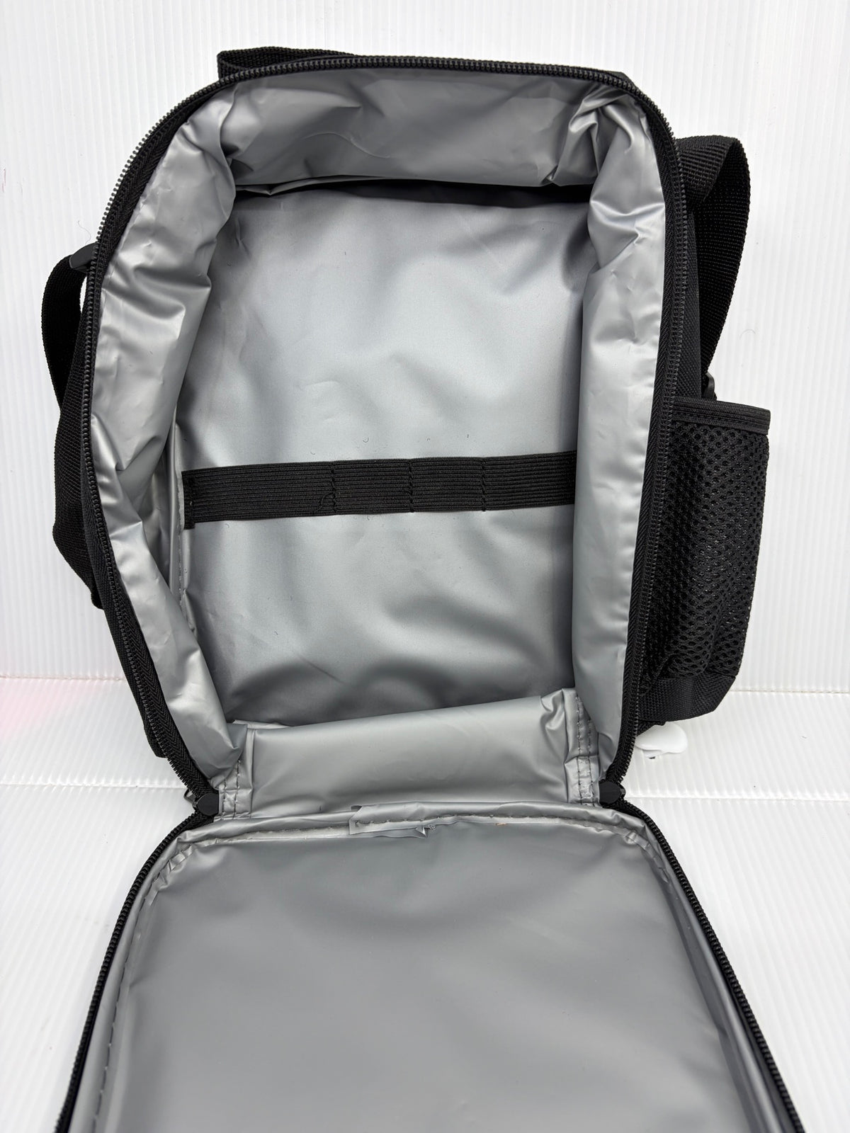Insulated lunch bag interior open showing silver lining, elastic keeper strap and side mesh pocket