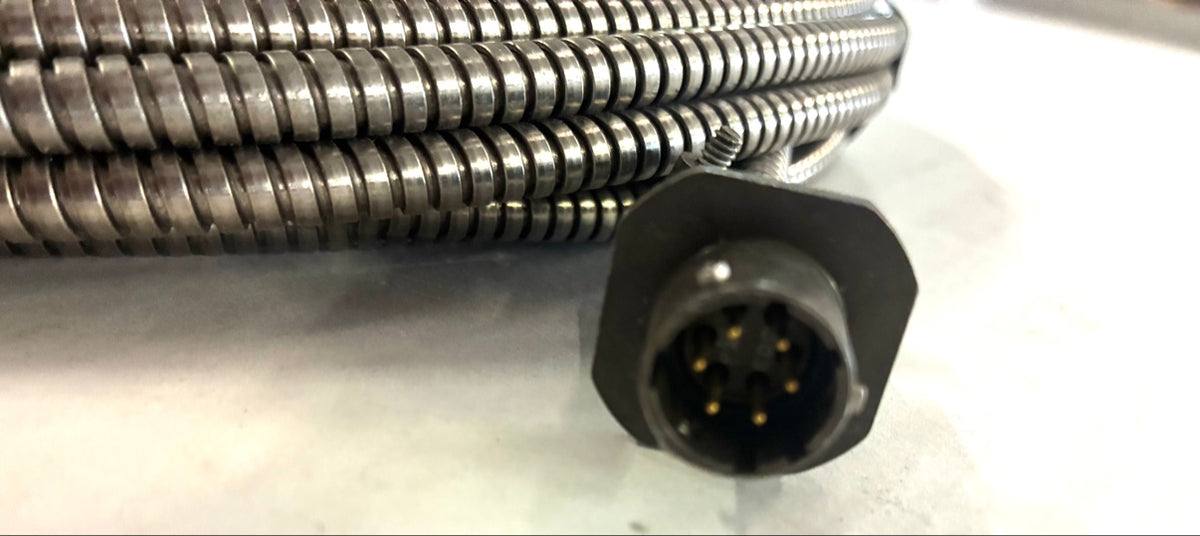 Close-up of 6-pin male circular connector showing six gold pins and flange shell on armored cable