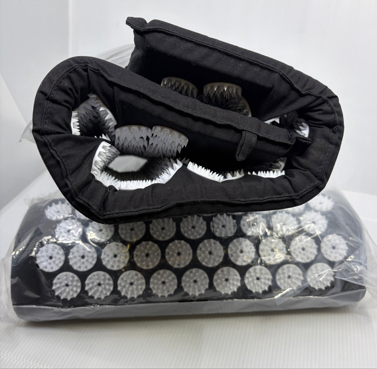ProsourceFit black acupressure mat rolled showing white pressure discs and cotton cover, pillow behind