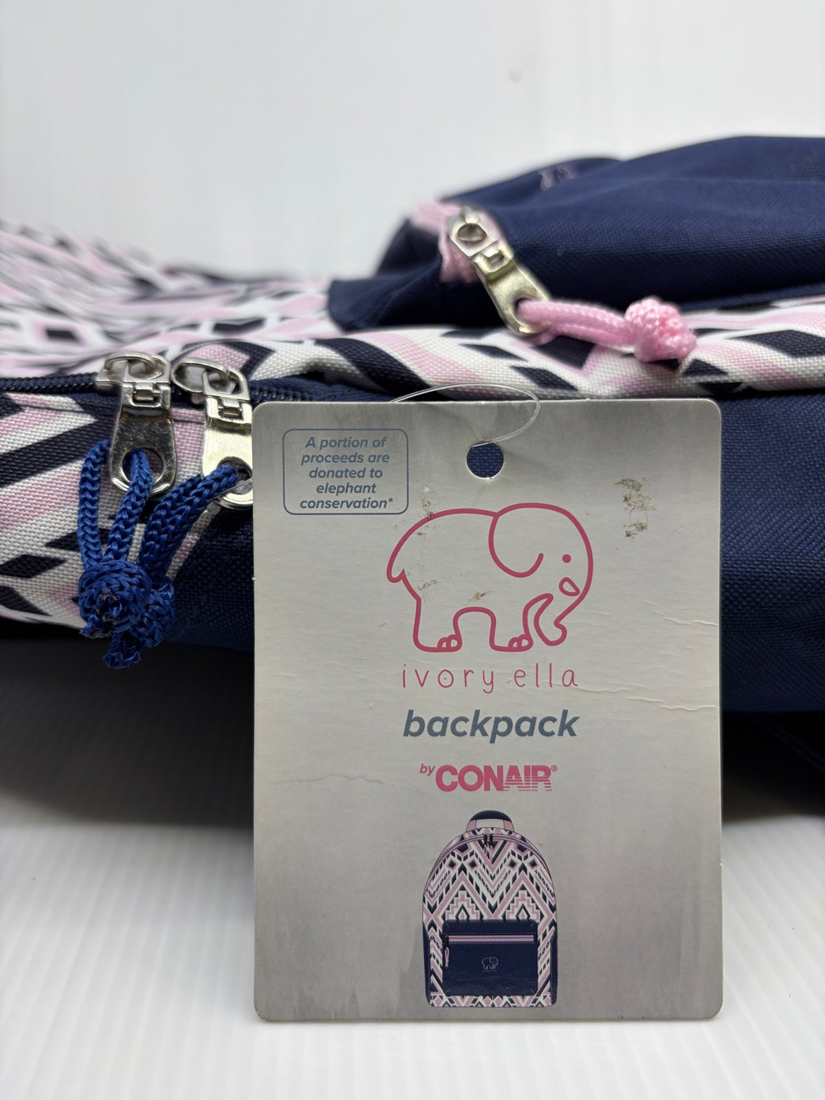 Ivory Ella backpack hangtag by Conair showing elephant logo and elephant conservation donation text, with zipper pulls