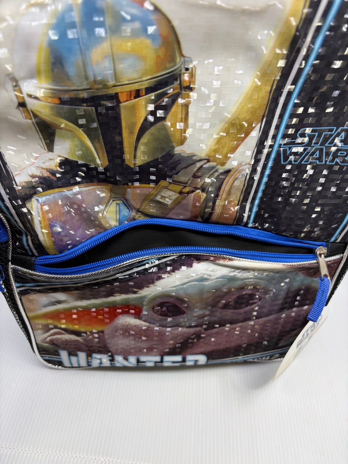 Detail of the glossy holographic front panel and open front zip pocket with blue zipper on the Mandalorian Grogu backpack