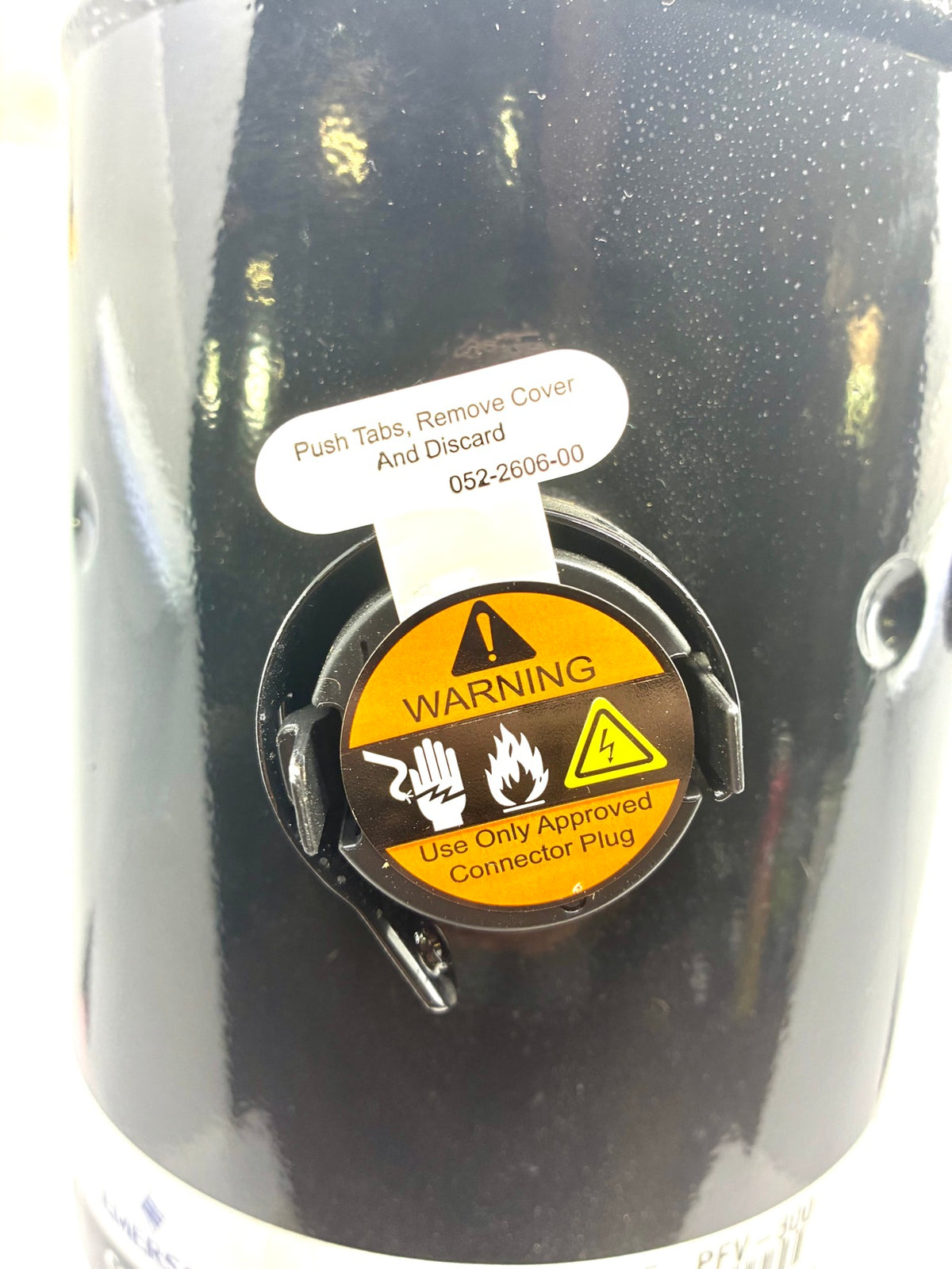 Close-up of Copeland scroll compressor electrical terminal cover with factory warning label and push tab tag still in place