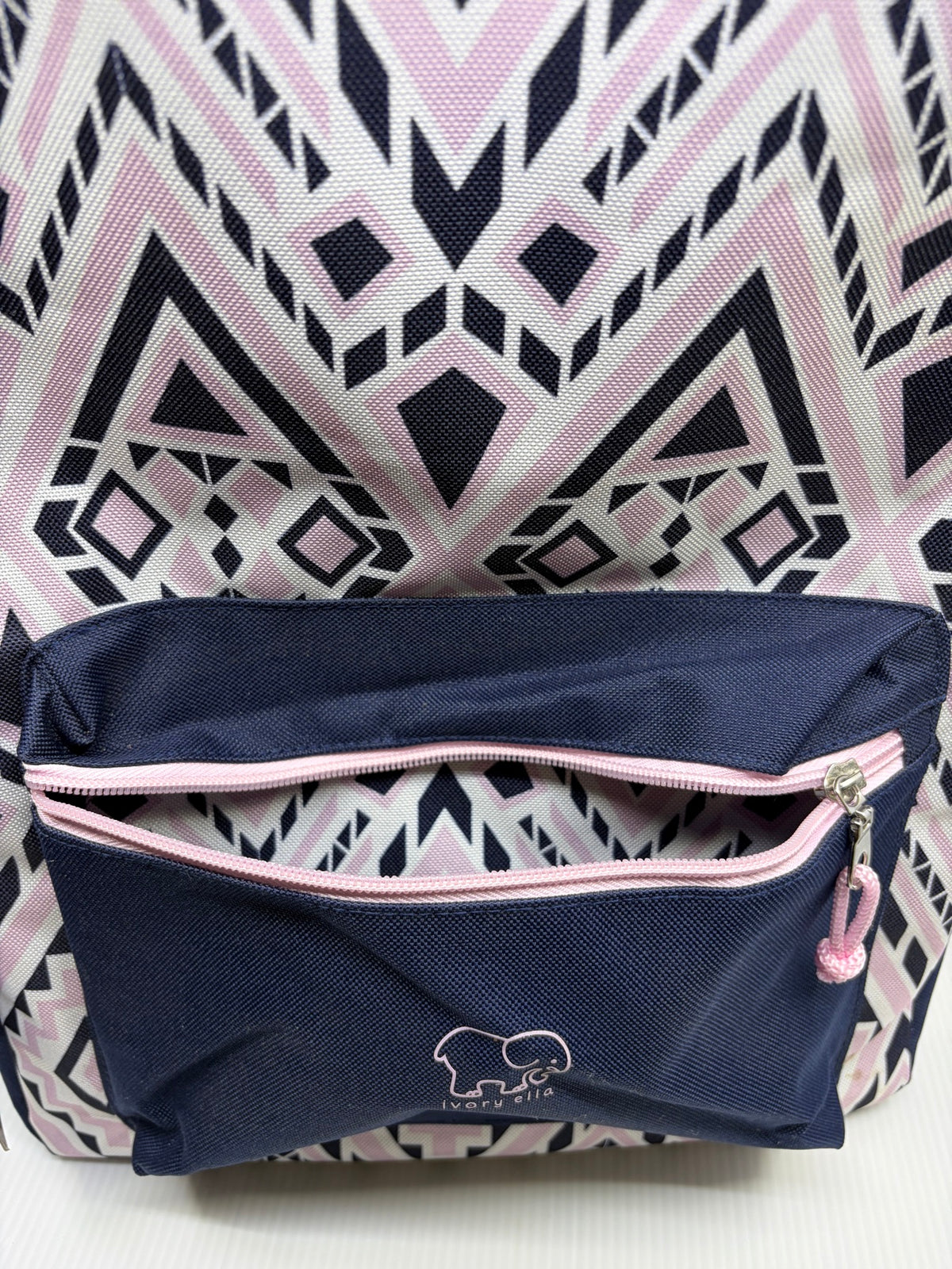 Front zip pocket open on the Ivory Ella backpack showing geometric pattern lining and pink zipper, small spots at lower right edge