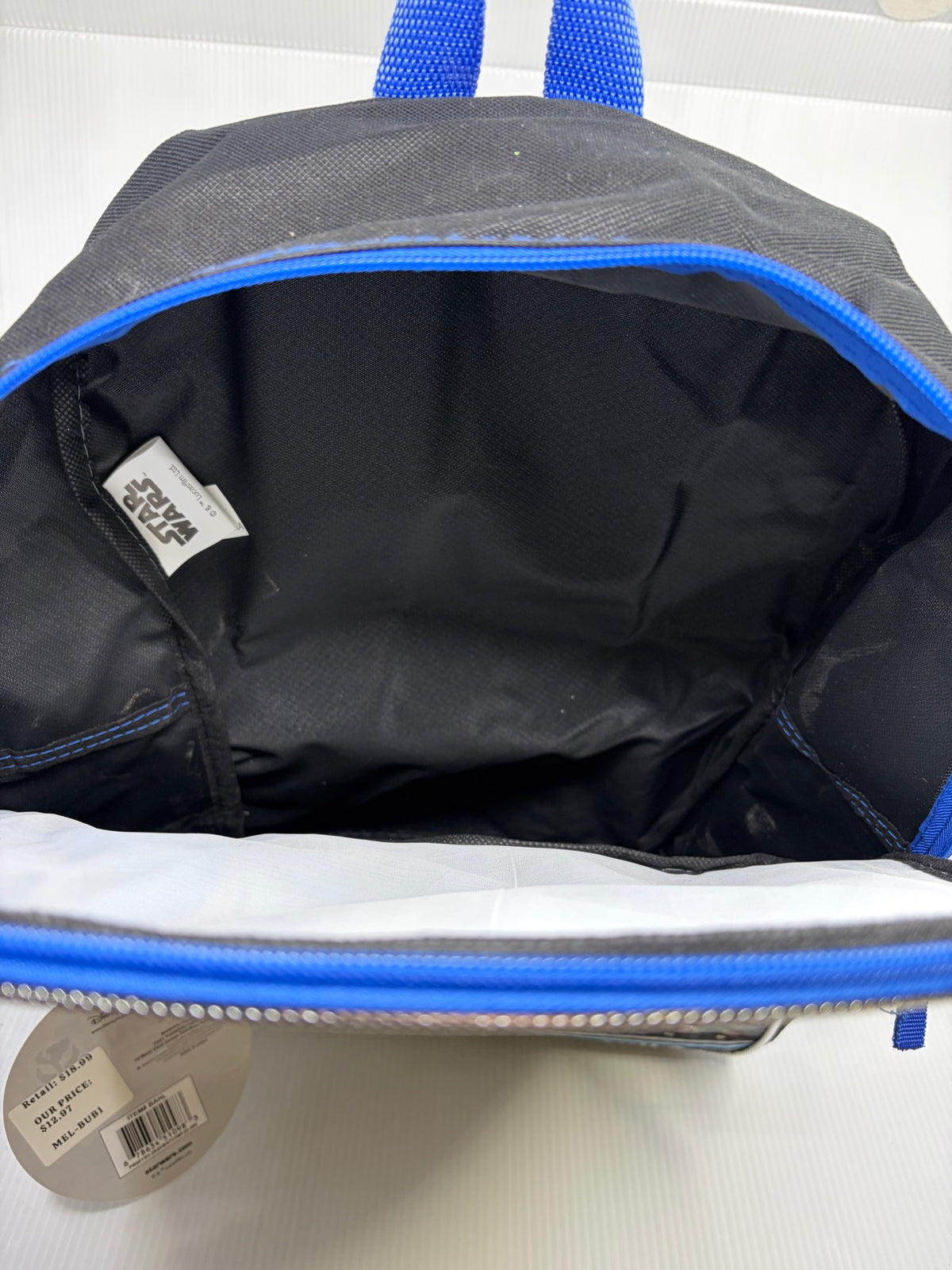 Interior of the Mandalorian backpack main compartment showing black lining and Star Wars Lucasfilm label, with the back of the hangtag and its UPC and retail sticker below
