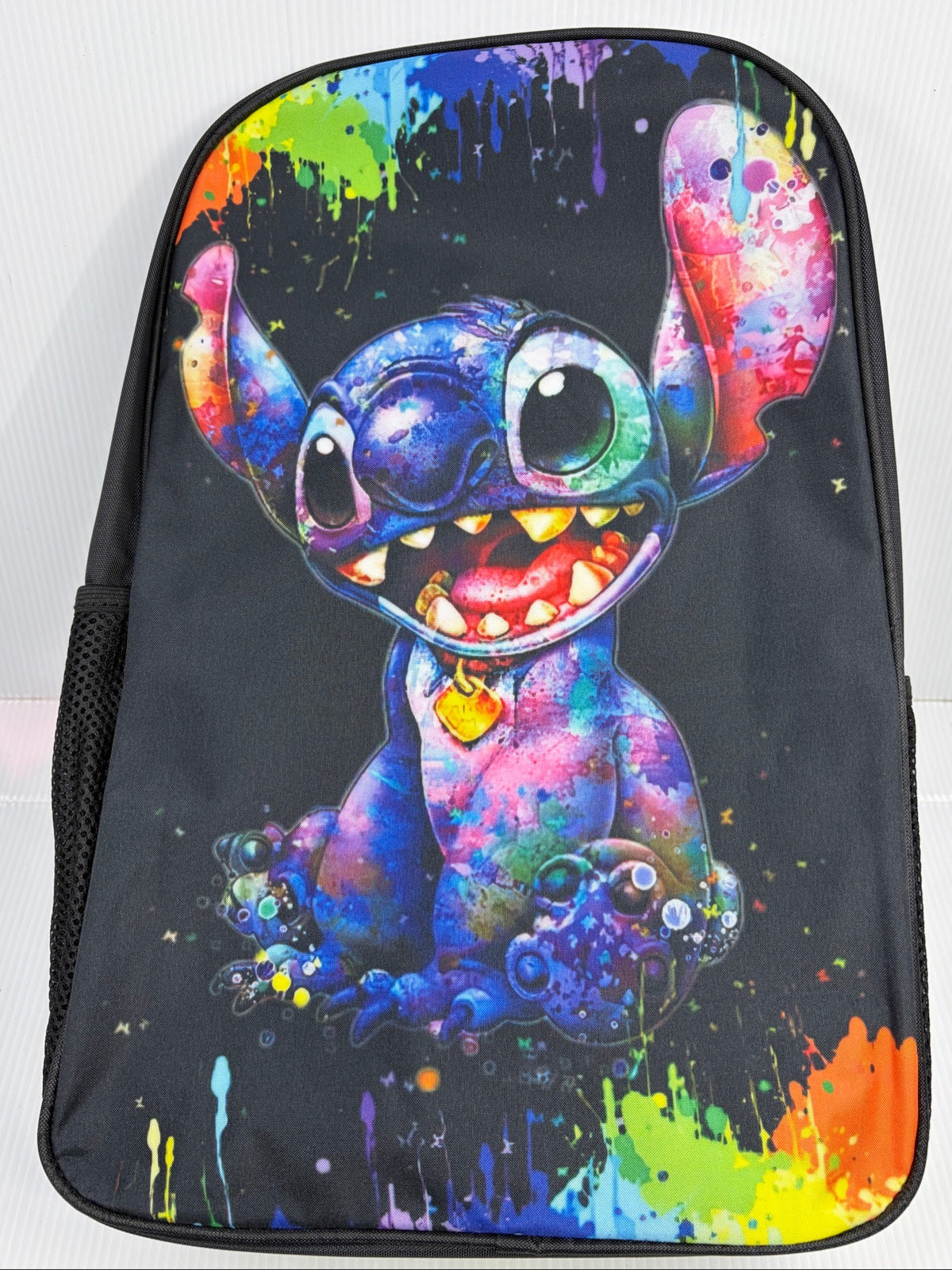 Backpack front alone showing full Stitch paint splatter artwork and side mesh pocket