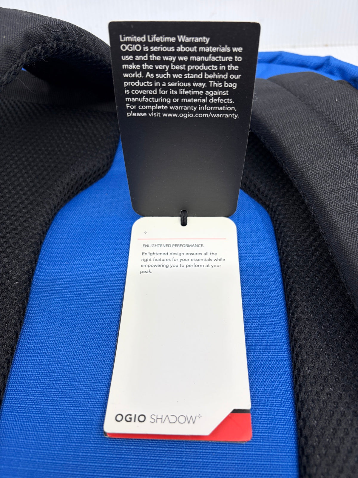 OGIO hangtag back showing Limited Lifetime Warranty text and OGIO Shadow Enlightened Performance branding