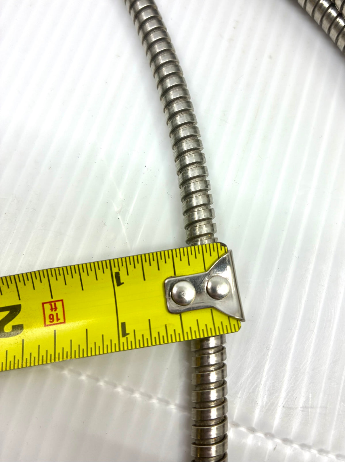 Tape measure across the interlocked metal armor showing approx. 1/4 inch armor outside diameter
