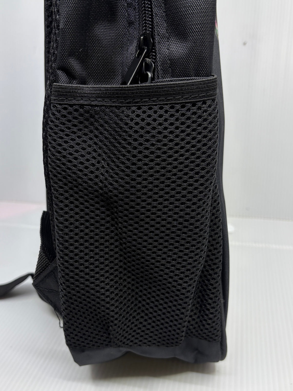 Opposite side view of the backpack showing mesh pocket and dual zipper pulls
