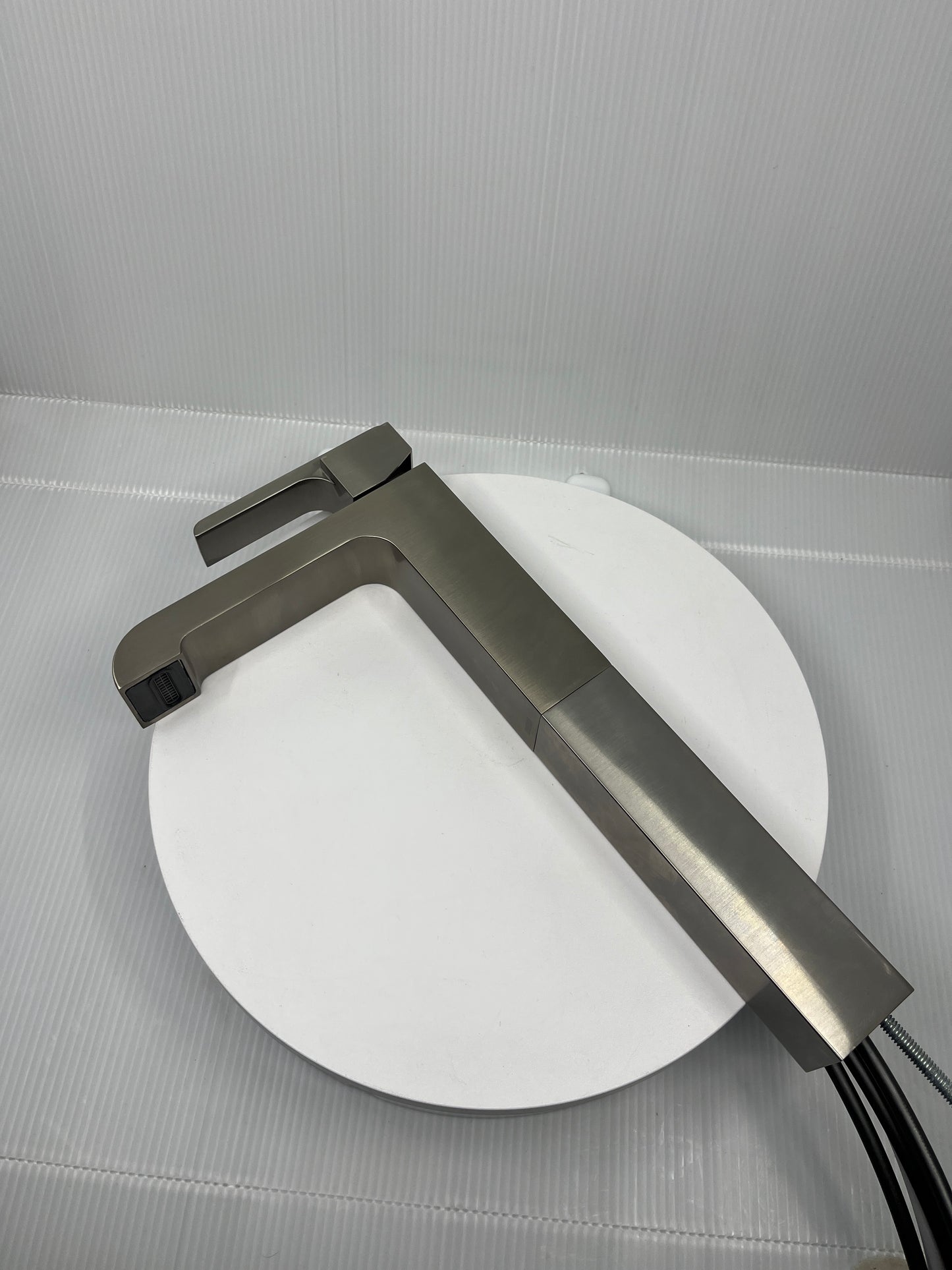 Stainless Steel single handle faucet on a white circular object with a gray background.