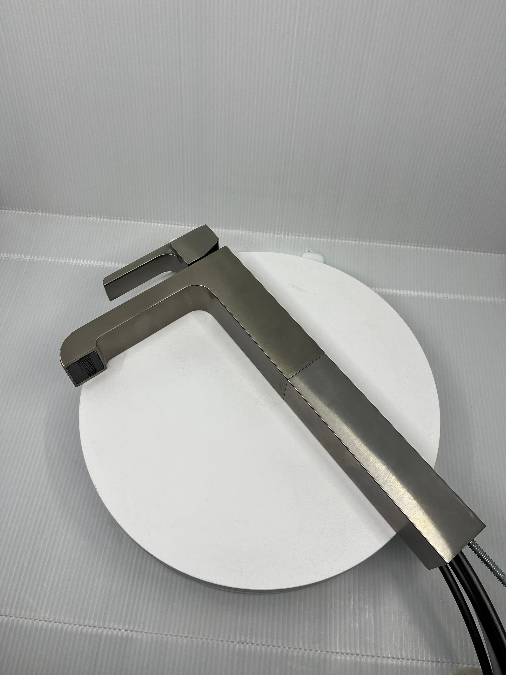 Stainless Steel single handle faucet on a white circular object with a gray background.