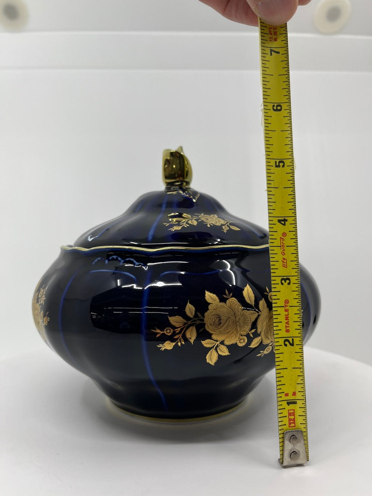 Blue decorative container with hand painted gold floral patterns with a measuring tape for scale on a white background.