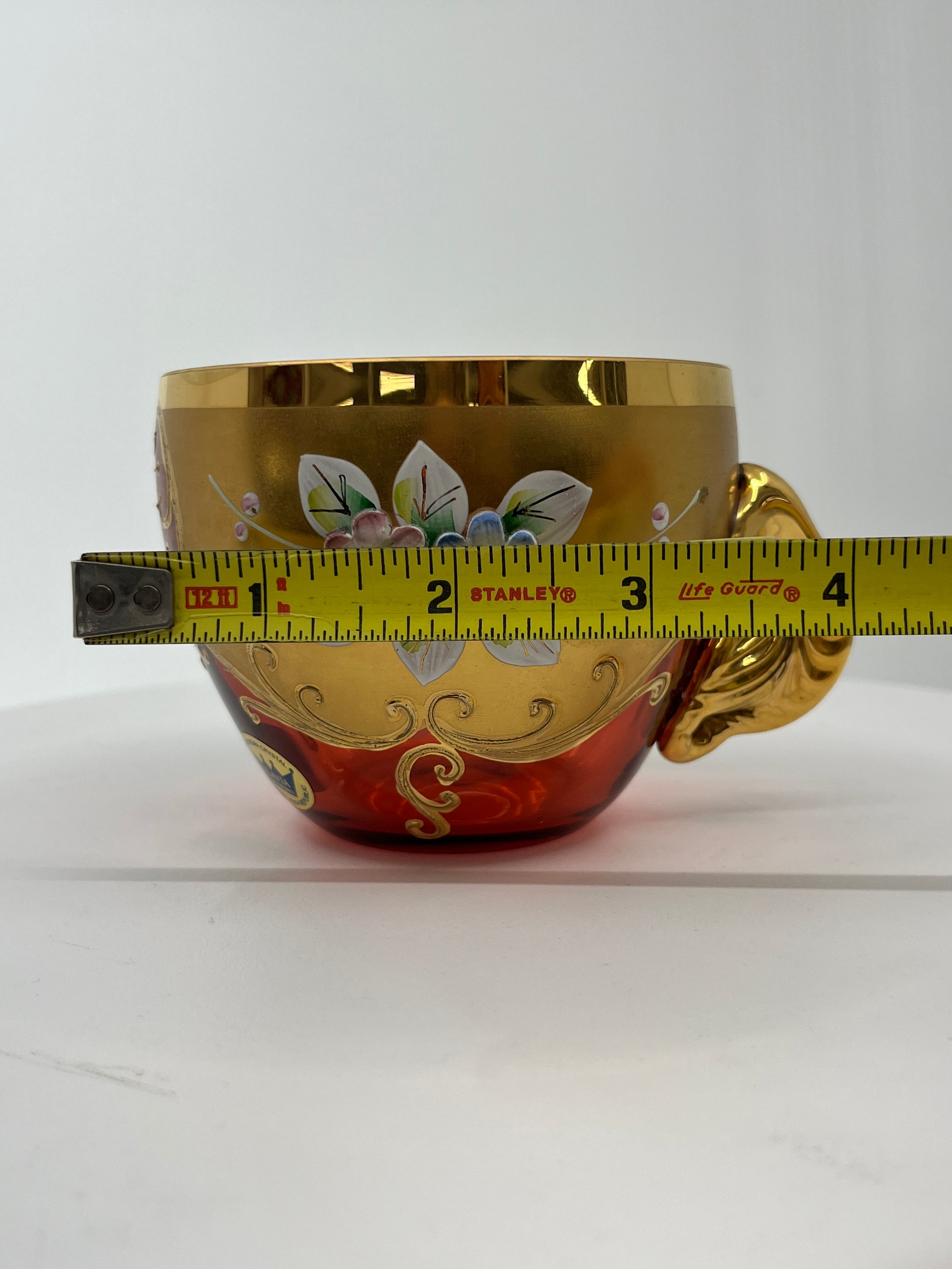 Decorative glass punchbowl teacup with floral designs and a measuring tape indicating its width.