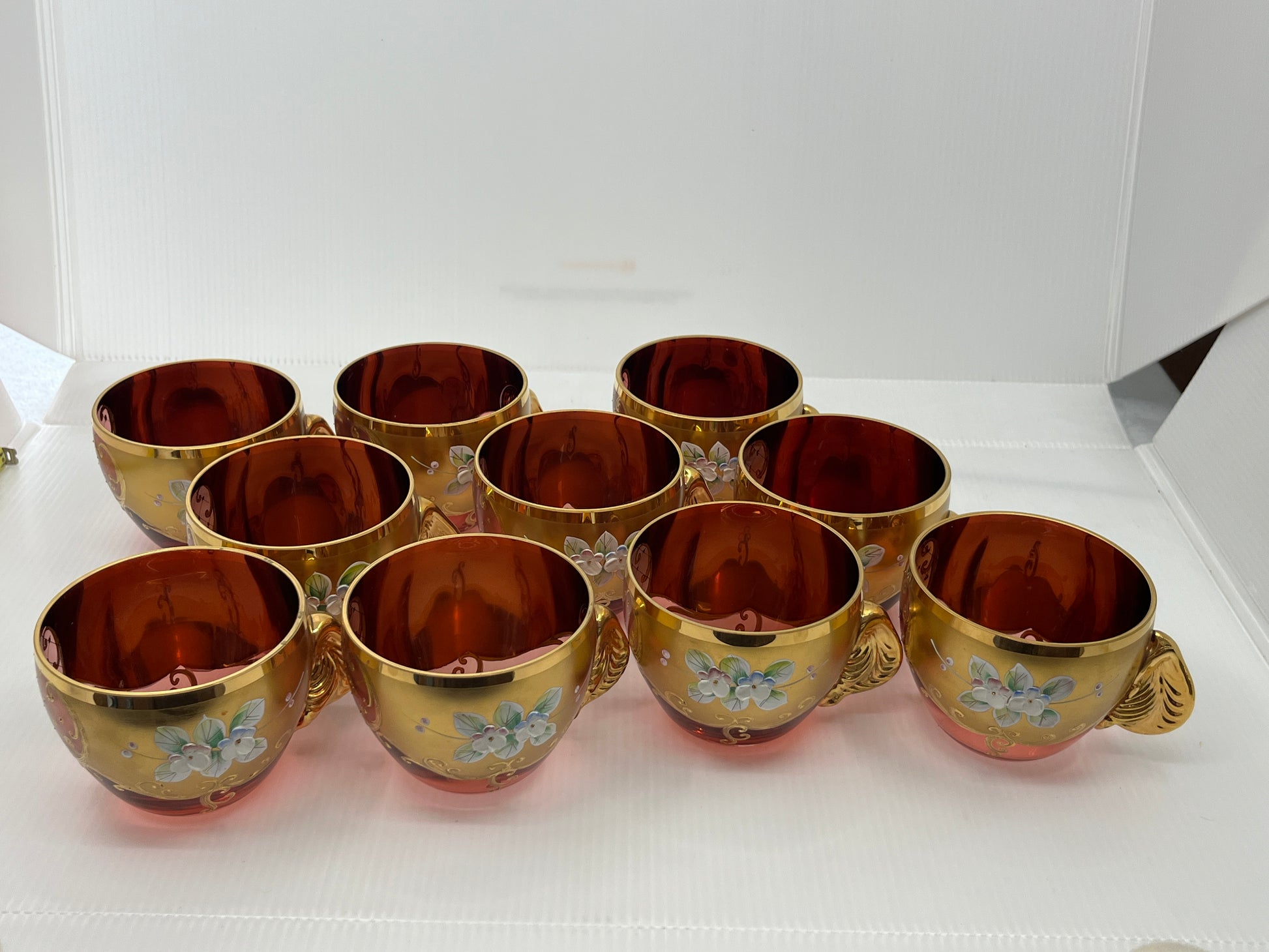 Set of gold-rimmed glass cups with floral designs on a white surface.