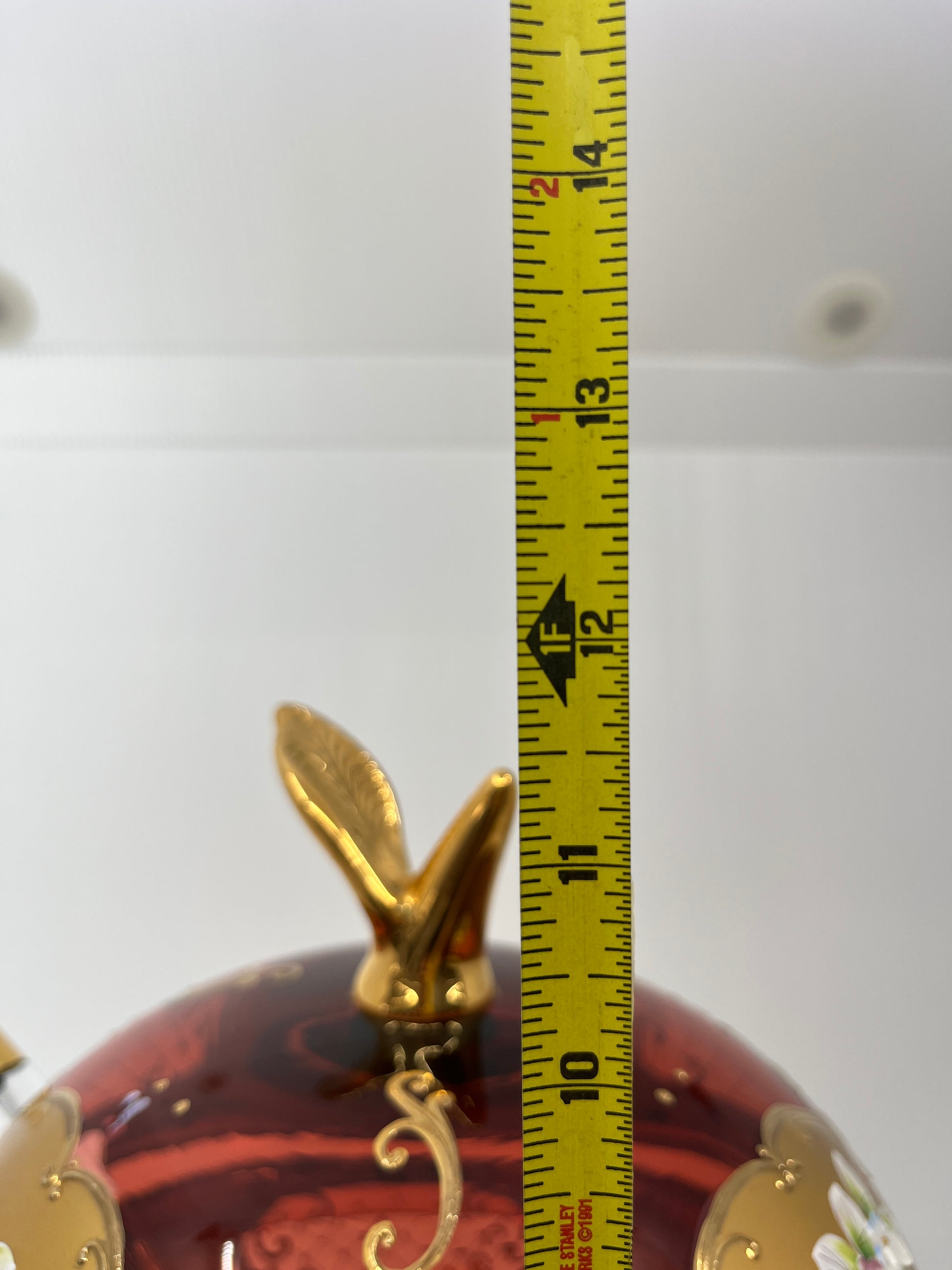 Decorative punchbowl lid with a gold leaf figure and measuring tape for scale on a white background