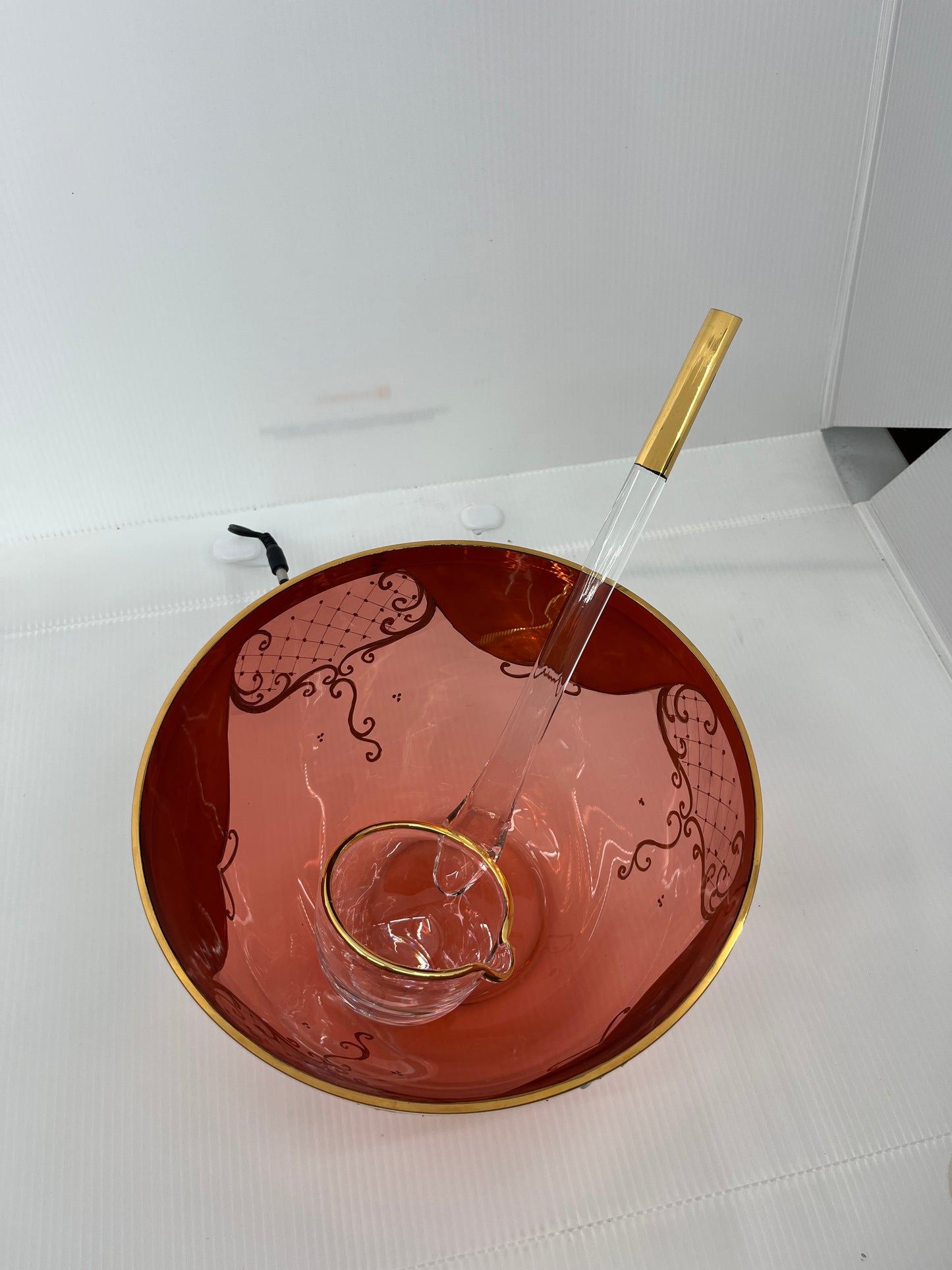 Decorative red punch bowl with gold rim and glass clear handle ladle on a white background