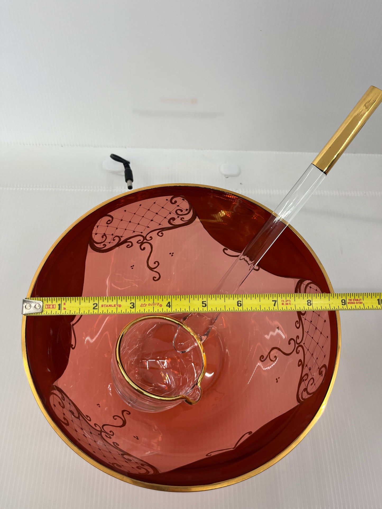 Decorative glass punch bowl with a measuring tape for scale on a plain background.