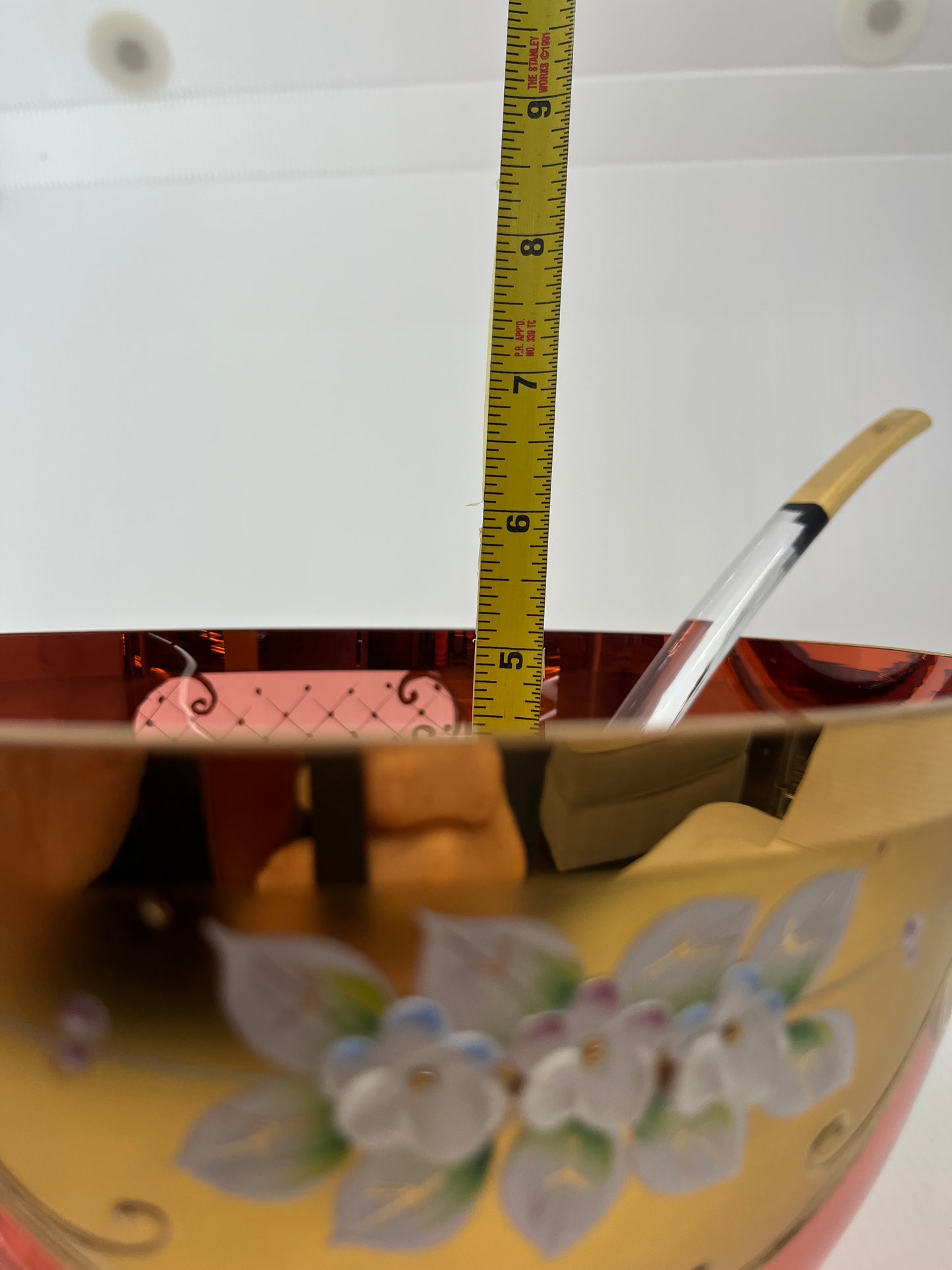 Close-up of a measuring tape with a glass ladle and decorative punch bowl in the background.